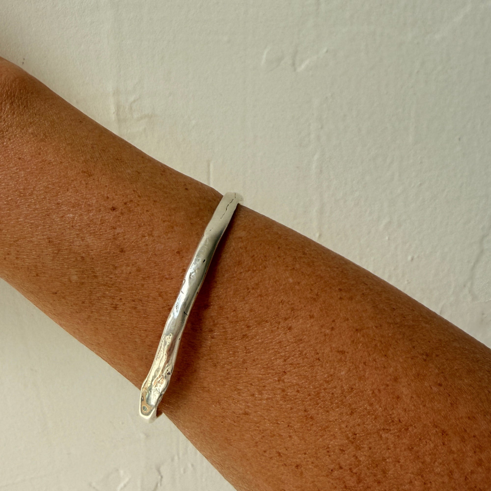 Silver bracelet on a wrist against a light gray background